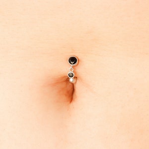 Può includere: Un piercing per l'ombelico in argento con tre gemme rotonde nere.