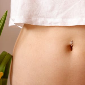 May include: A close-up of a person's midriff with a small, silver belly button ring.