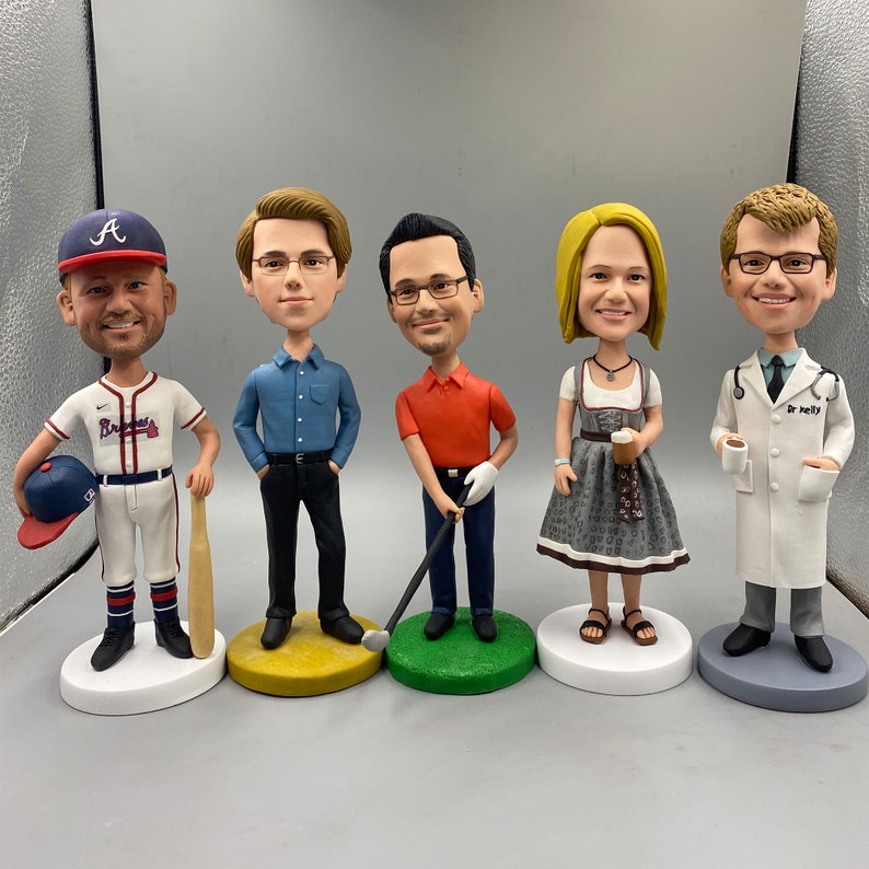 May include: Five personalized figurines of people, each standing on a round base. The figurines are painted in realistic detail and depict a baseball player, a man with glasses, a woman with long hair, a man with a golf club, and a man in a white coat.