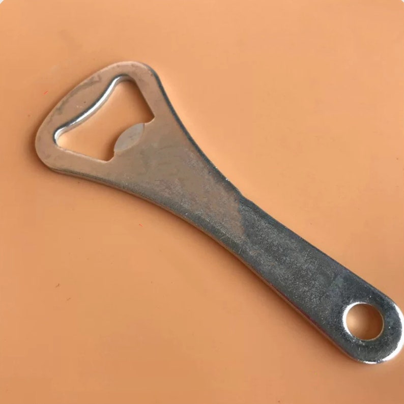 May include: A silver bottle opener with a simple design. The opener has a small hole at the end of the handle.