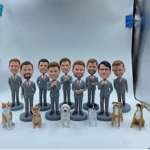May include: A group of ten custom-made figurines of men wearing gray suits and pink ties. Each figurine has a different hairstyle and facial features. The figurines are arranged in a row with their names written below them. There are also five figurines of dogs in front of the men. The dogs are all different breeds and colors.