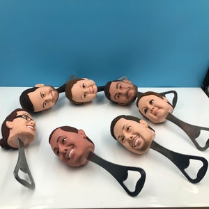 May include: A set of seven bottle openers with personalized faces. Each opener is made of metal and has a bottle opener on one end and a face on the other end.
