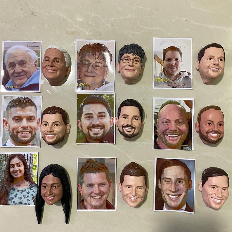 May include: A collection of 18 small, realistic portrait sculptures of people's faces. The sculptures are made of a light brown material and are displayed on a white surface.