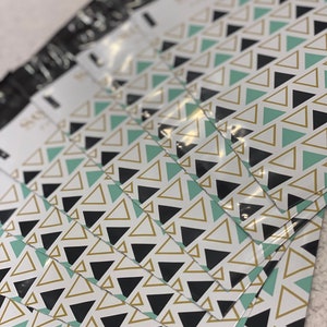 May include: A stack of white and black poly mailer envelopes with a repeating geometric triangle pattern in black, gold, and teal. The envelopes are angled, showing the patterned design.