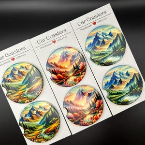 May include: Set of six car coasters featuring a scenic mountain landscape with a lake and trees. The coasters are round and have a glossy finish. The text "Car Coasters" and "Handmade with love" is printed on the white background.