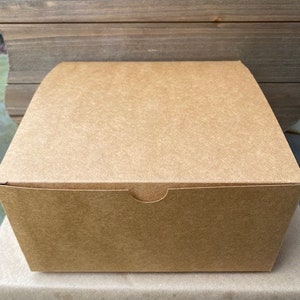 May include: A brown cardboard box with a flap on the top. The box is sitting on a brown surface.