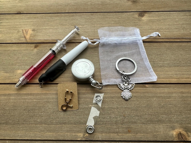 May include: A set of medical themed gifts including a retractable badge reel, a stethoscope charm, a syringe pen, a white marker, and a silver angel keychain in a white organza bag.