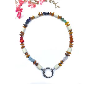 Puede incluir: Un collar de piedras preciosas de colores arcoíris con cuentas blancas y un cierre plateado.