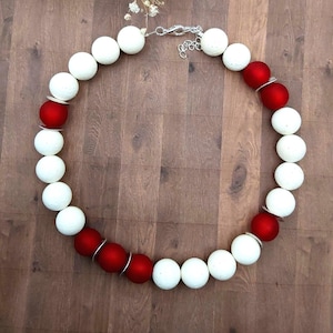 May include: A necklace composed of alternating white and red spherical beads. The necklace is secured with a silver-coloured chain and clasp. The beads are arranged in a circular design, creating a striking and noticeable accessory.