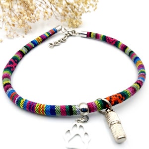 Könnte beinhalten: Ein farbenfrohes gewebtes Hundehalsband mit einem silbernen Pfotenanhänger und einem silbernen Röhrenanhänger. Das Halsband ist aus einem dicken, strapazierfähigen Material gefertigt und perfekt für Hunde aller Größen.