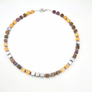 May include: A necklace made of square-shaped beads in shades of brown, orange, and silver. The necklace has a silver clasp.