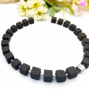 May include: A black lava rock necklace with silver metal connectors. The necklace is made of square-shaped beads.