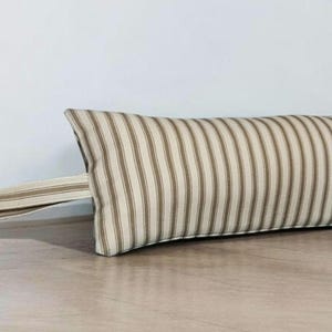 May include: A brown and white striped doorstop with a loop handle. The doorstop is made of fabric and is designed to prevent doors from slamming.