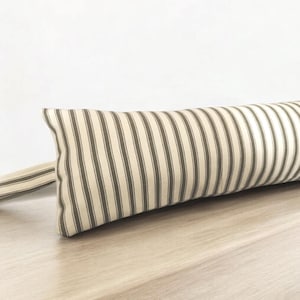 May include: A long, cylindrical cushion with a white and brown striped fabric cover. The cushion is lying on a light brown wooden surface.