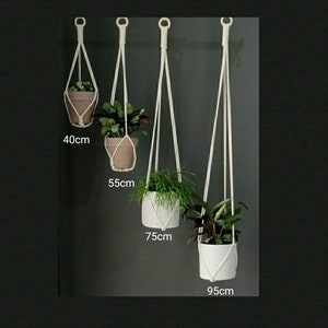 May include: Four white macrame plant hangers with different lengths, 40cm, 55cm, 75cm, and 95cm, hanging from a wall with potted plants.