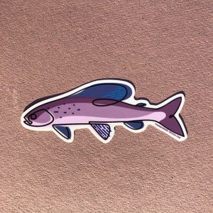 Puede incluir: Una pegatina de pescado ilustrada en morado y azul con un contorno blanco. El pez tiene un diseño detallado con un cuerpo texturizado y una aleta. La pegatina tiene el texto "Thunderbird Design.com" en la esquina inferior derecha.
