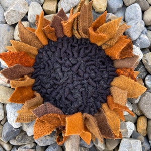 May include: A handmade felt sunflower with brown, orange, and black petals. The sunflower is attached to a wooden stick.