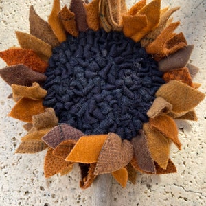 May include: A handmade felt sunflower with a brown, orange, and black color scheme. The sunflower has a textured center and a wooden stem.