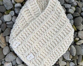 May include: A cream-colored chunky knit cowl scarf featuring a textured stitch pattern and three large, rectangular white buttons attached along the overlapping front edge, creating a secure and adjustable fit for the neck area.