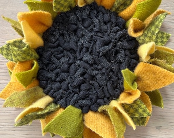May include: A felt sunflower with yellow and green petals and a black center. The sunflower is attached to a brown stick.