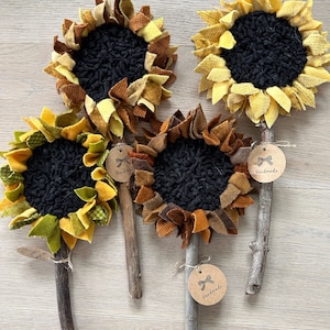 May include: Four handmade felt sunflower decorations with brown sticks and "Handmade" tags. The sunflowers are made with different shades of yellow, orange, brown, and green felt.