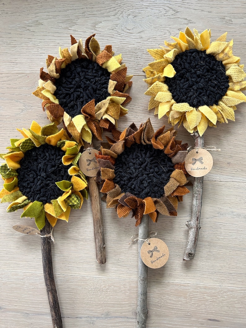 May include: Four handmade felt sunflower decorations with brown sticks and "Handmade" tags. The sunflowers are made with different shades of yellow, orange, brown, and green felt.