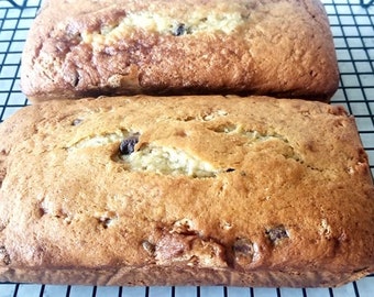 Può includere: Due pani di banana, appena sfornati e in raffreddamento su una griglia. Il pane è dorato e ha una crosta leggermente croccante.