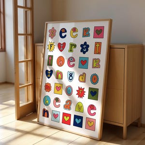 May include: A colourful alphabet poster with letters and hearts in a grid pattern. The letters are in a variety of colours and styles, and the hearts are red. The poster is framed in a light wood frame.