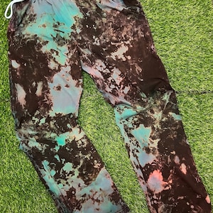 May include: Black tie-dye sweatpants with a blue and pink pattern. The sweatpants have a drawstring waist and a relaxed fit.