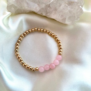 Pode incluir: Um bracelete de contas douradas com uma fila de contas de quartzo rosa.