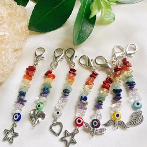May include: Seven rainbow charm keychains with different charms, including a star, a heart, a dragonfly, and a wing. Each charm is attached to a beaded chain with an evil eye bead at the bottom.