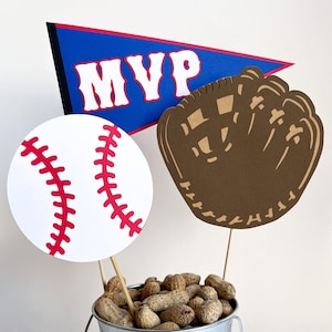 May include: A baseball themed centerpiece with a white baseball, a brown baseball glove, and a blue pennant with the word "MVP" in red letters. The items are placed in a silver bucket filled with peanuts.
