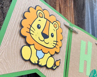 May include: A green and brown banner with a cartoon lion illustration. The lion is orange and yellow with a white face and a black nose. The banner has the letter "H" on it.