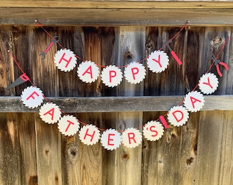 Puede incluir: Una pancarta blanca y roja con las palabras "Happy Father's Day" escritas en formas de hojas de sierra. La pancarta está atada con una cuerda roja y tiene pequeñas herramientas negras y rojas colgando de ella.