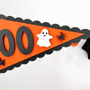 May include: Orange and black Halloween banner with the word "BOO" in black letters. The banner is decorated with a white ghost and black spiders.