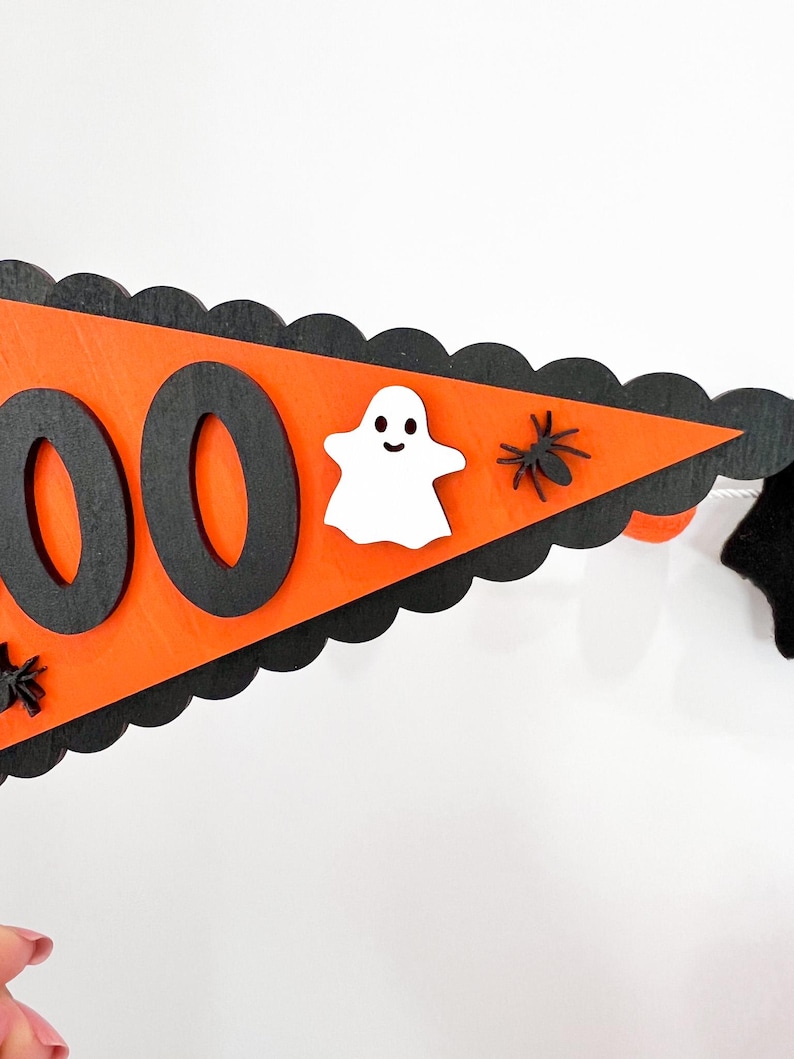 May include: Orange and black Halloween banner with the word "BOO" in black letters. The banner is decorated with a white ghost and black spiders.
