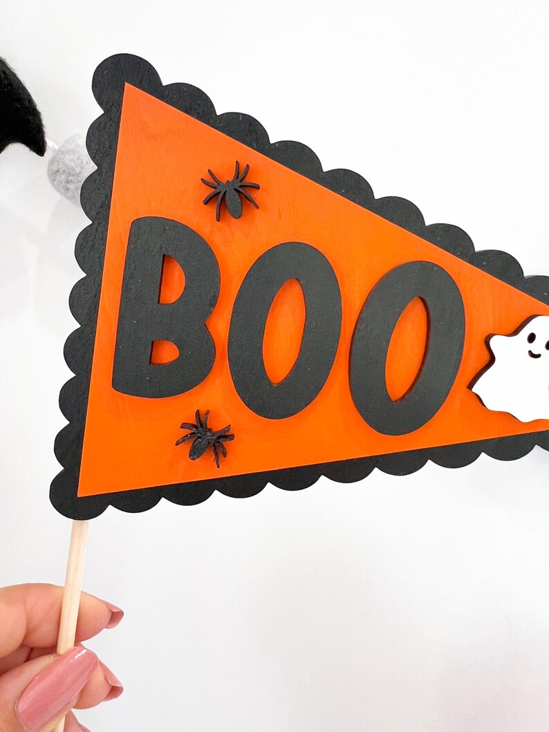 May include: Orange and black Halloween banner with the word "BOO" in black letters. The banner has a scalloped edge and is decorated with black spiders and a white ghost.