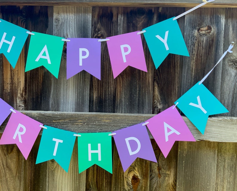 May include: A banner with the words "Happy Birthday" in white letters on alternating pink, purple, and teal triangular flags.