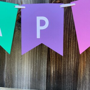 May include: A purple banner with the letter "P" in white, hanging on a wooden fence. The banner is part of a larger banner that spells out the word "Happy".