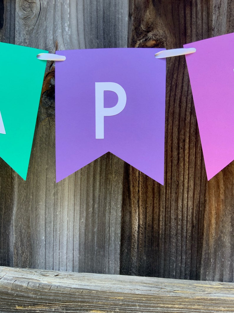 May include: A purple banner with the letter "P" in white, hanging on a wooden fence. The banner is part of a larger banner that spells out the word "Happy".