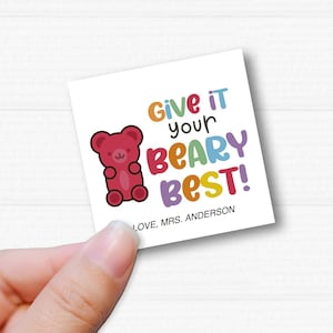 May include: A white card with a red gummy bear illustration and the text "Give it your Beary Best!" in rainbow colors. The text "Love, Mrs. Anderson" is printed below the illustration.