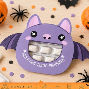 May include: A purple bat-shaped paper card holder featuring a cutout window displaying a blister pack of white gum. The card has pink inner ears, black eyes, and the white text "HAVE A FANG-TASTIC-HALLOWEEN" printed below the gum pack.
