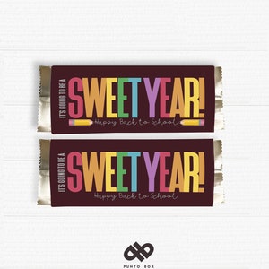 Può includere: Due involucri di barrette di cioccolato con sfondo marrone e il testo "IT'S GOING TO BE A SWEET YEAR! Happy Back to School" in lettere colorate. Una matita gialla è disegnata accanto al testo.