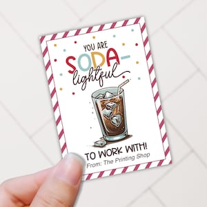 May include: A white card with red and white stripes on the border. The card has a colorful illustration of a glass of iced soda with a straw. The text on the card reads "You are soda-lightful to work with! From: The Printing Shop."