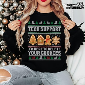 Peut inclure: Sweat-shirt noir avec un motif festif. Le texte "TECH SUPPORT" est au-dessus d'une maison en pain d'épices, d'un bonhomme en pain d'épices, d'un sapin de Noël et d'un flocon de neige. En dessous, le texte dit "I'M HERE TO DELETE YOUR COOKIES".