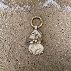 Pode incluir: Uma caneca de cerâmica branca com uma alça preta e o texto "But First, Coffee" em negrito preto. A caneca está sobre um fundo desfocado, sugerindo um ambiente acolhedor.