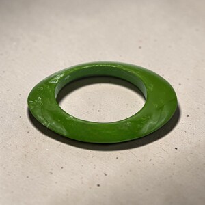 Peut inclure: Une bague verte vif de forme ovale. La bague a une finition lisse et brillante avec de légères variations de couleur. Le design est simple et moderne, adapté au quotidien. La bague est faite d'un matériau solide.