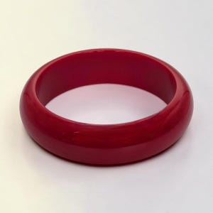 Peut inclure: Un bracelet jonc rouge uni. Le bracelet rond est d'une teinte rouge vif avec une finition brillante. Le bijou est un accessoire simple mais élégant.