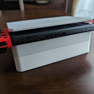 Può includere: Una console Nintendo Switch bianca e nera con un controller Joy-Con rosso e nero attaccato a ciascun lato. La console è appoggiata su una docking station bianca.