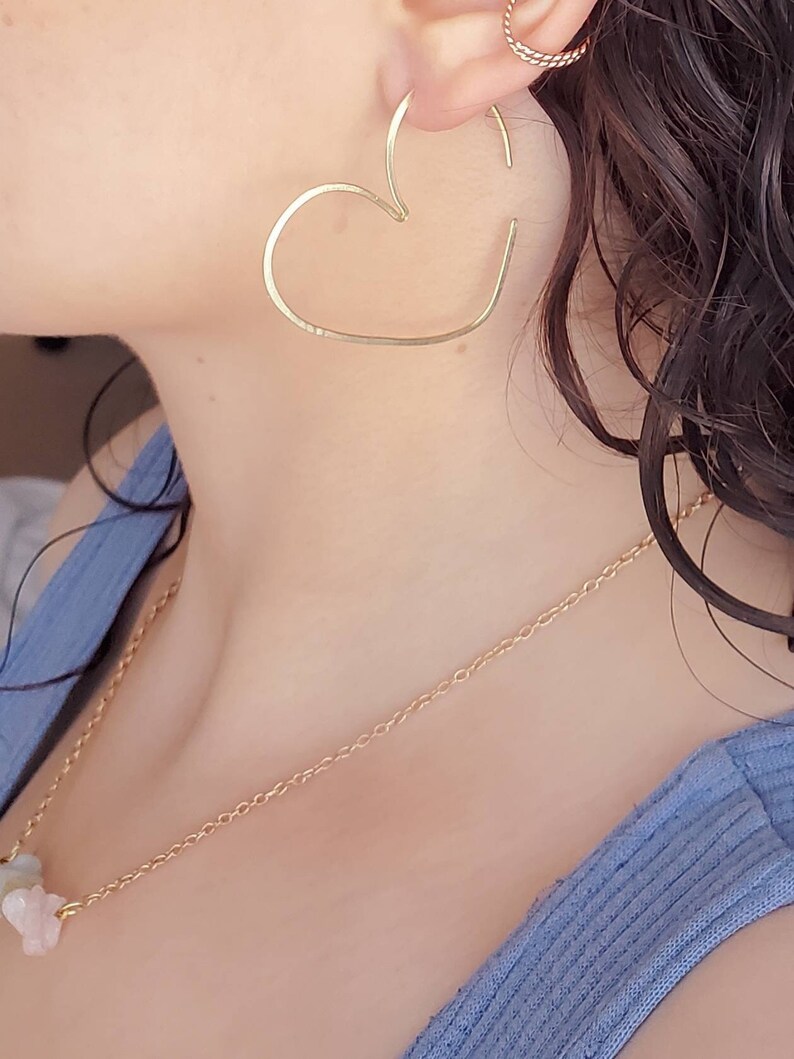May include: A gold heart-shaped hoop earring with a delicate chain necklace featuring pastel-colored stones.
